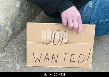 disoccupato seduto a terra con un cartello di cartone dire lavoro voluto Foto Stock