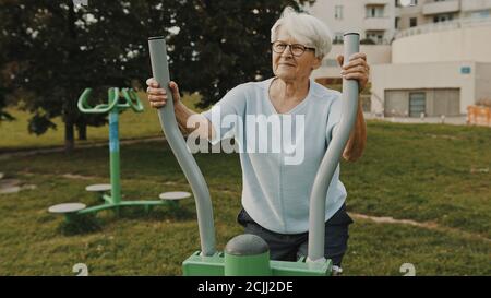 Granny capelli grigi che si esercita all'esterno palestra parco giochi attrezzature. Foto di alta qualità Foto Stock