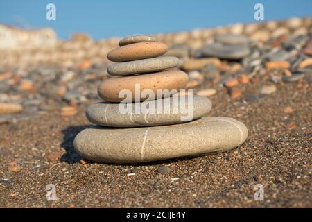 torre di pietra fatta a mano su una spiaggia di ghiaia e sabbia. Piramide di ciottoli grigi. Zen scultura. Carta da parati. Concetto di vacanza estiva. Foto Stock