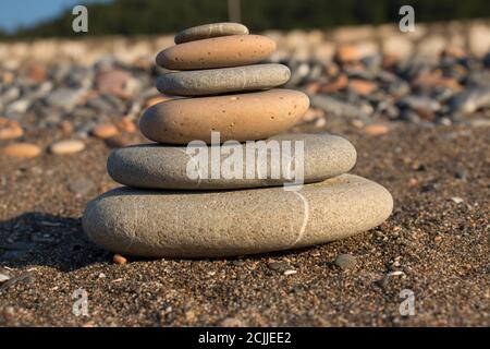 torre di pietra fatta a mano su una spiaggia di ghiaia e sabbia. Piramide di ciottoli grigi. Zen scultura. Carta da parati. Concetto di vacanza estiva. Foto Stock