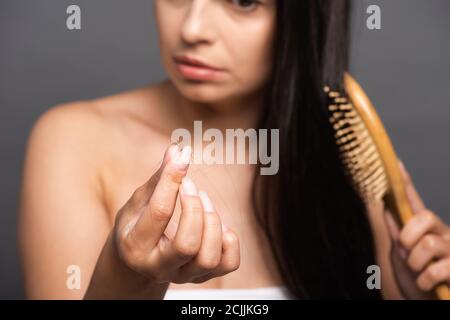 fuoco selettivo della donna della spazzoletta che tiene i capelli persi mentre spazzolando isolato su nero Foto Stock