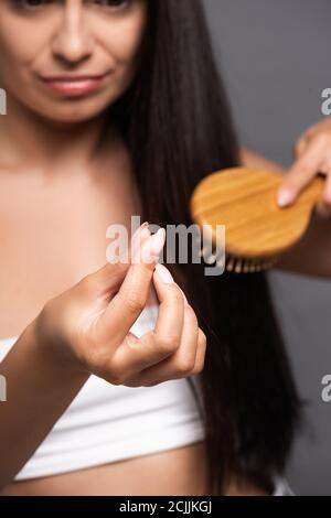 fuoco selettivo della donna della spazzoletta che tiene i capelli persi mentre spazzolando isolato su nero Foto Stock