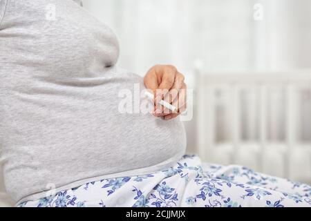 Una donna incinta con una sigaretta in mano. Primo piano di mano e pancia. Il concetto di dipendenza da nicotina e la salute delle donne. Foto Stock