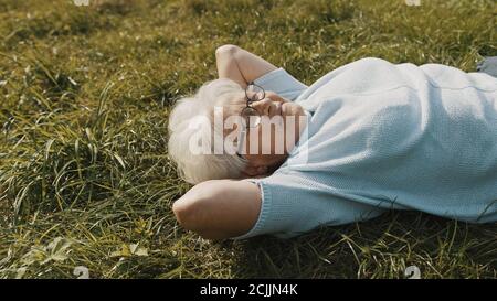 Nonna fresca sdraiata sull'erba con le mani sotto la testa. Riposo in natura. Foto di alta qualità Foto Stock