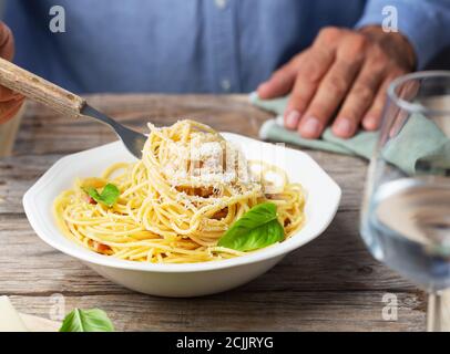 L'uomo in una camicia blu sta mangiando nella carbonara italiana della pasta fatta con l'uovo, il formaggio duro, guanciale di maiale stagionato o la pancetta e pepe nero Foto Stock