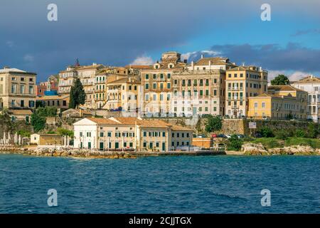 Isola di Corfù/Grecia - 7 maggio 2019: Paesaggio urbano di Kerkyra - baia di mare con acque turchesi calme, vecchie case storiche, costa rocciosa e nuvole grigie sul Foto Stock