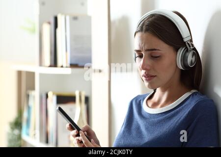 Triste teen lamentando l'ascolto di musica guardando giù e piangendo a casa Foto Stock