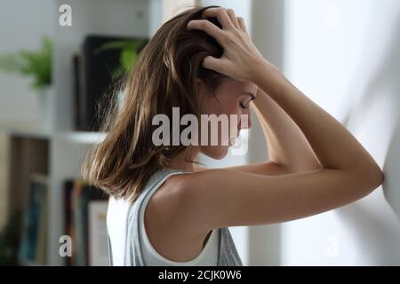 Vista laterale ritratto di una donna triste che si lamenta appoggiandosi un muro a casa di notte Foto Stock