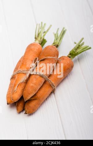 carote fresche legate con corda su tavolo di legno bianco Foto Stock