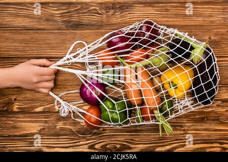 vista tagliata di donna che tiene borsa a corda con fresco maturo verdure su tavola di legno Foto Stock