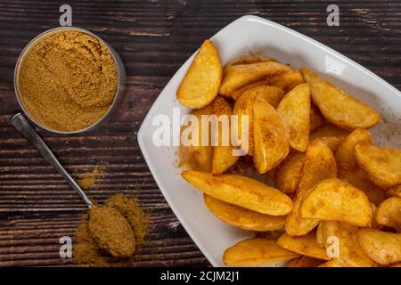 Patate a zeppa piccanti su piatto bianco su tavolo di legno Foto Stock