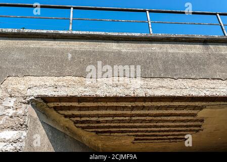 Viadotto ferroviario danneggiato con soffitto fessurato, rinforzo arrugginito visibile e acciaio. Foto Stock