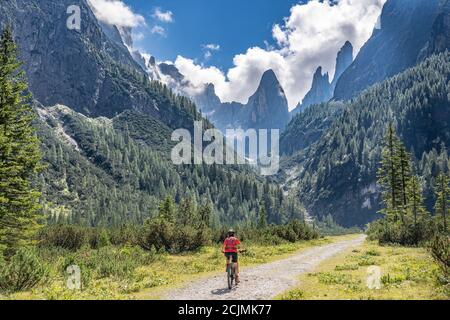 Bella donna anziana che cavalca la sua mountain bike elettrica nella Val di Fischlein nelle Dolomiti di Sesto con la famosa meridiana di Sextan sullo sfondo, tre cime Foto Stock