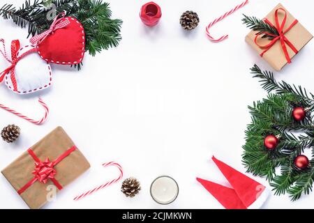 Cornice di Natale fatta di rami di abete, caramelle rosse, coni, cappelli di Babbo Natale, regalo in una scatola, decorazioni. Natale o Capodanno. Disposizione piatta, parte superiore Foto Stock