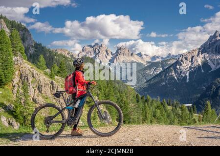 Bella e attiva donna anziana che cavalca la sua mountain bike elettrica sull'altopiano di Prato Piazzo nelle tre cime dolomitiche , silhouette rocciosa di Foto Stock