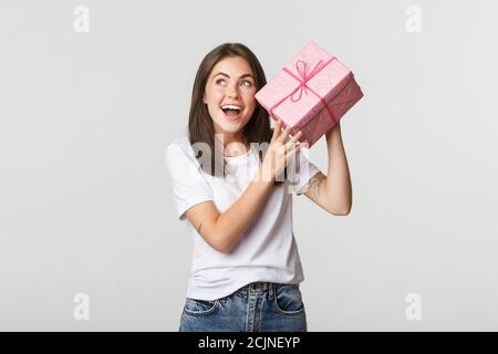 Intrigato felice compleanno ragazza scuotendo scatola regalo per scoprire che cosa dentro Foto Stock