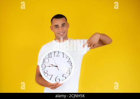 Bell'uomo latino-americano giovane che tiene grande orologio guardando positivo e felice Foto Stock