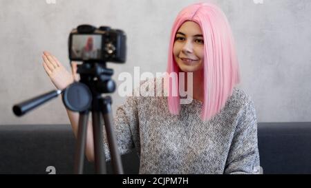 Felice blogger ragazza in parrucca rosa davanti alla fotocamera su un treppiede. Registra un video blog e comunica con gli abbonati sui social network Foto Stock