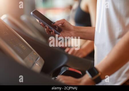 Primo piano di una donna che utilizza il suo telefono cellulare durante l'allenamento tapis roulant in palestra Foto Stock