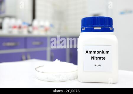 Fuoco selettivo di una bottiglia di nitrato di ammonio in una bottiglia di plastica accanto a una capsula di Petri con palline bianche all'interno di un fondo di laboratorio. Foto Stock