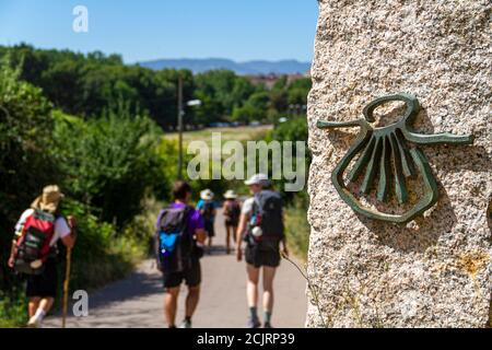 Pellegrini sulla rotta del Camino de Santiago (Via di San Giacomo) passando accanto allo shell dello scaloppo che segna la via Foto Stock