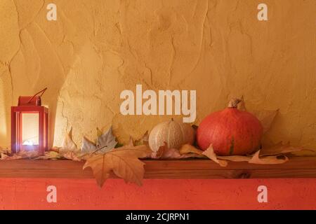 Zucca arancione, candela bruciante in lanterna, foglie di caduta asciutte su tavola di legno, sfondo giallo della parete. Halloween vintage sfondo. Mokup per Halloween Foto Stock