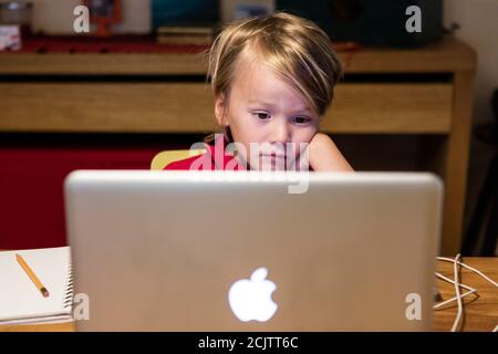 Un ragazzo sembra poco interessato a guardare un computer portatile mentre si impara a distanza seduto al tavolo da pranzo a casa, a Miami, Florida, Stati Uniti Foto Stock