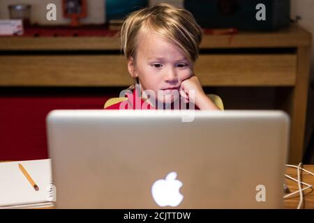 Un ragazzo si annoia a guardare un computer portatile mentre impara a distanza seduto al tavolo da pranzo a casa, a Miami, Florida, USA Foto Stock