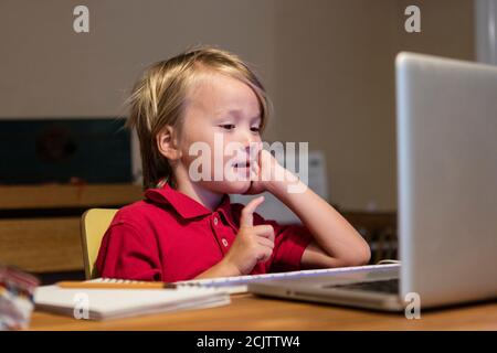 Un ragazzo impara a distanza su un computer portatile mentre si siede al tavolo da pranzo a casa, a Miami, Florida, USA Foto Stock