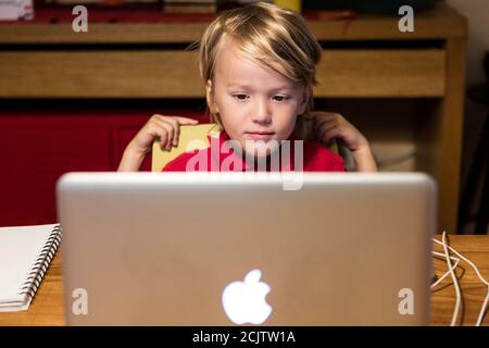 Un ragazzo si siede di fronte a un computer guardando il suo insegnante di asilo su un computer portatile mentre si siede al tavolo da pranzo a casa, a Miami, Florida, USA Foto Stock