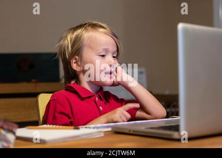 Un ragazzino parla con il suo insegnante di asilo su un computer portatile mentre si sta seduto al tavolo da pranzo a casa, a Miami, Florida, USA Foto Stock