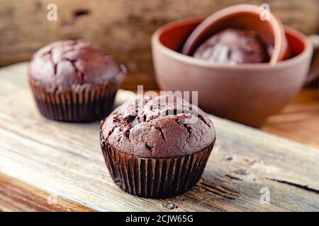 Cupcake al cioccolato sul tavolo in stile rustico. Muffin al cioccolato appena sfornati senza top su sfondo di legno scuro. Cupcake senza crema di condimento Foto Stock