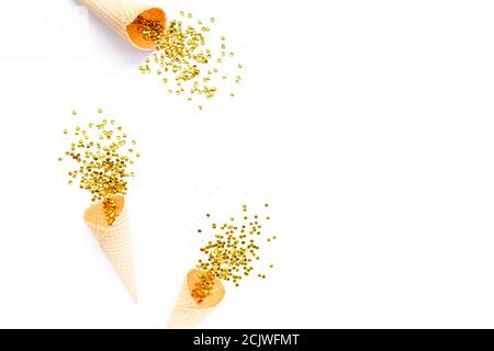 Coni di cialde gialli con nappina di confetti dorati isolati su sfondo bianco. Piatto, vista dall'alto, festivo minimo. Concetto di festa e celebrazione. Foto Stock