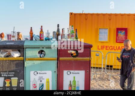 Svuotare le bottiglie nei contenitori dei rifiuti accanto a un contenitore salvavita Sul lungomare di Brighton in estate Foto Stock