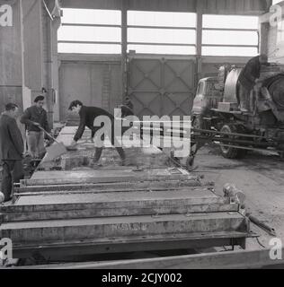 Anni '60, storici, lavoratori all'interno di un'unità industriale alta che fabbricano pannelli prefabbricati in calcestruzzo, utilizzando calcestruzzo umido in stampi riutilizzabili, Inghilterra, Regno Unito. In quest'epoca, questo tipo di prodotto da costruzione era in domanda poiché gli edifici ad alto aumento erano messi nelle città principali intorno al regno unito e la forma 'Brutual' di architettura era in moda. Costruendo i pannelli prefusi fuori sede si risparmia sia sulla manodopera che sui materiali rispetto ai metodi di costruzione tradizionali che utilizzano mattoni e muratori. Foto Stock