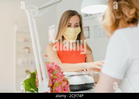 Donna nel salone delle unghie che riceve manicure che indossa una faccia maschera Foto Stock