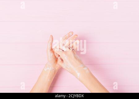 Vista dall'alto delle mani femminili nel processo di procedura passo-passo di lavaggio delle mani con saponette sulla pelle su sfondo rosa. Foto Stock