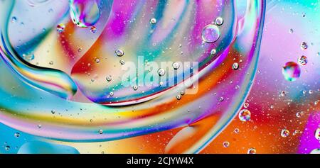 Iridescente sfondo macro astratto di gocce di olio in movimento sul superficie dell'acqua con bolle d'aria all'interno Foto Stock