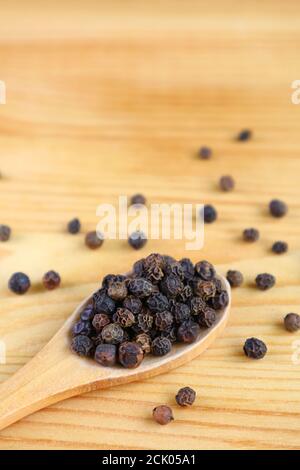 Mucchio di peppercorne nere su cucchiaio di legno con alcuni sparsi su tavolo di legno Foto Stock