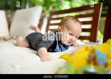 Cute bambino ragazzo di tre mesi che gioca con i suoi giocattoli colorati all'aperto. Bambino durante il periodo di pancia. Carino bambino imparare a strisciare. Foto Stock