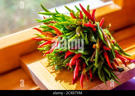 Un fascio di peperoncini verdi e rossi appena raccolti sul davanzale in legno alla luce del giorno. Colorato sfondo di cibo naturale Foto Stock