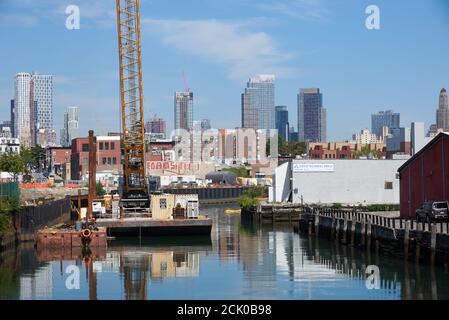 Vista del canale Gowanus a Brooklyn, NY con una chiatta e una gru da costruzione. Sullo sfondo sono i grattacieli del centro di Brooklyn. Foto Stock