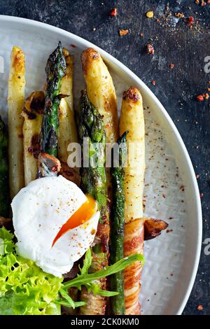 Prima colazione di asparagi cotti in spezie con pancetta, uova in camicia e insalata croccante. Contorno per pranzo e cena. Foto Stock