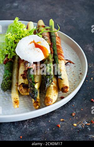 Prima colazione di asparagi cotti in spezie con pancetta, uova in camicia e insalata croccante. Contorno per pranzo e cena. Foto Stock