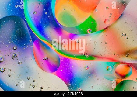 Iridescente sfondo macro astratto di gocce di olio in movimento sul superficie dell'acqua con bolle d'aria all'interno Foto Stock