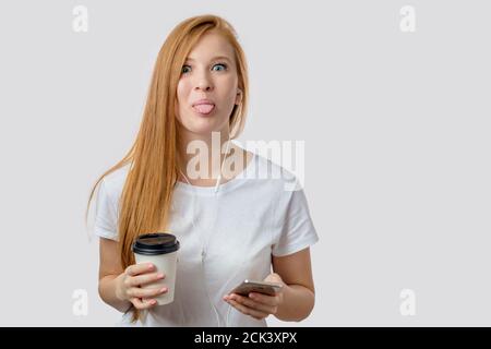 una donna splendida sta mettendo la lingua fuori mentre ascolta la musica e bevendo il tè. sfondo bianco isolato. spazio di copia. concetto di emozione Foto Stock