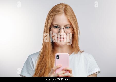 la ragazza sorprende dei capelli rossi sta guardando il telefono come sta leggendo qualcosa di interessante. scioccante notizie da friend.emotive femmina con sguardo stupito Foto Stock