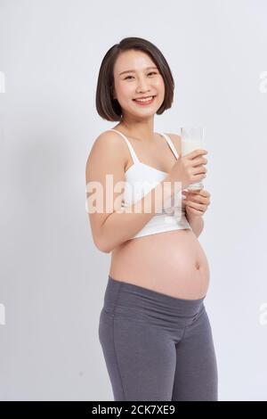 Giovane donna asiatica incinta con un bicchiere di latte in mano. Foto Stock