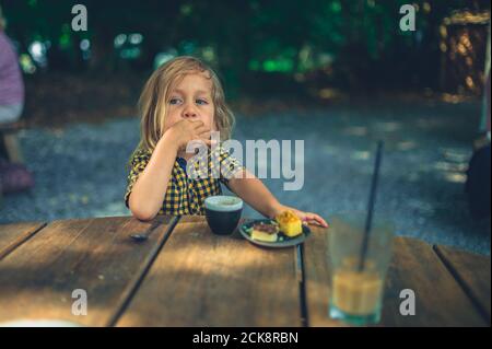 Un po' di preschooler sta bevendo caffè e mangiando torte all'aperto ad un tavolo da caffe' Foto Stock