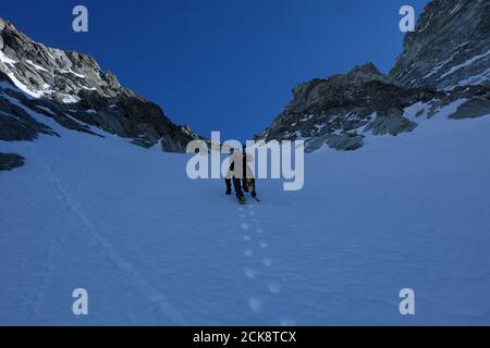 Scalata invernale con ramponi e ghiaccio, sci sul retro, couloir Anzévui, Aiguille de la TSA, Vallese, Svizzere Foto Stock